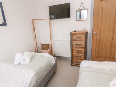 A bedroom with two beds, a wall-mounted TV, a wooden chest of drawers, a mirror, and a clothes rack at Tregenna House in St Ives