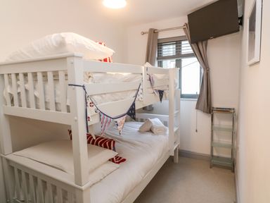 A bedroom with a white bunk bed a window with gray curtains and a wall mounted television at Tregenna House in St Ives