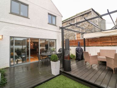 An outdoor patio with dining table and chairs a wicker seating set and a wooden pergola at Tregenna House in St Ives