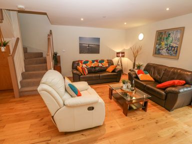 A living room with brown and white sofas a glass coffee table and a staircase at Barn End 9 Stad Clynnog in Newborough