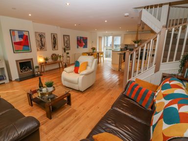 A living room with a leather sofa a white armchair a glass coffee table a staircase and a dining area at Barn End 9 Stad Clynnog Newborough