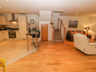 An open plan kitchen and living room with a staircase in the center and furniture at Barn End 9 Stad Clynnog in Newborough