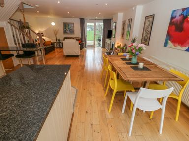 A living room and dining area with a wooden dining table and yellow and white chairs at Barn End 9 Stad Clynnog in Newborough