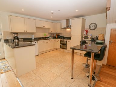 A kitchen with beige cabinets black countertops a stove a microwave and a small dining table with two chairs at Barn End 9 Stad Clynnog in Newborough