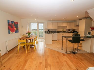 A kitchen and dining area with a wooden table and yellow chairs a kitchen island with black stools and white cabinets at Barn End 9 Stad Clynnog Newborough