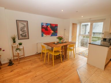 A dining area with a wooden table and yellow chairs next to a door and kitchen at Barn End 9 Stad Clynnog in Newborough