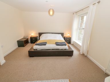A bedroom with a double bed two bedside tables with lamps a window with white curtains and a carpeted floor at Barn End 9 Stad Clynnog in Newborough