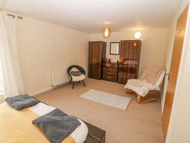 A bedroom with a bed, two chairs, two wardrobes, a dresser with a mirror, and a small rug on the carpeted floor at Barn End 9 Stad Clynnog Newborough