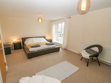 A bedroom with a bed bedside tables lamps a window a chair and a rug at Barn End 9 Stad Clynnog in Newborough
