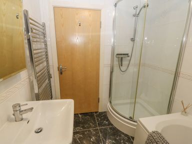 A bathroom with a sink a wooden door a glass shower enclosure and a heated towel rail at Barn End 9 Stad Clynnog in Newborough