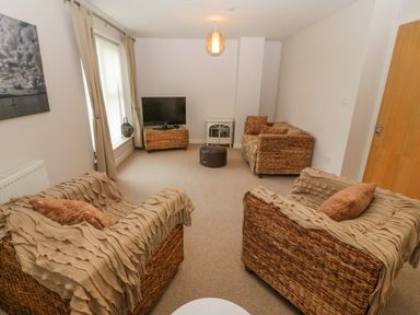 A living room with two armchairs covered with blankets a sofa a television on a wicker stand and a small stove at Barn End 9 Stad Clynnog in Newborough
