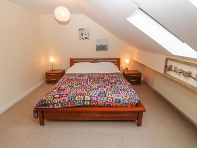 A bedroom with a wooden bed covered with a colorful quilt bedside tables with lamps and decorative wall art at Barn End 9 Stad Clynnog in Newborough