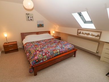 A bedroom with a wooden bed and colorful blanket under a skylight window at Barn End 9 Stad Clynnog in Newborough