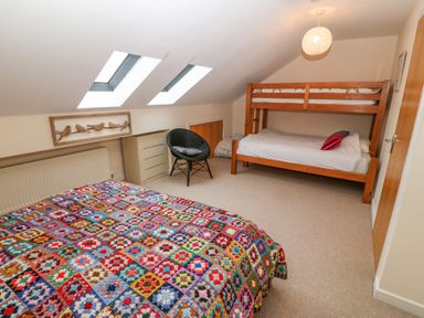A bedroom with a double bed covered with a colorful quilt a bunk bed a black chair two skylight windows and a chest of drawers at Barn End 9 Stad Clynnog in Newborough