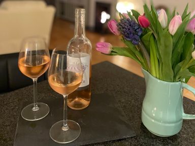 Two glasses of rose wine and a bottle on a black placemat next to a light blue pitcher with flowers at Barn End 9 Stad Clynnog in Newborough