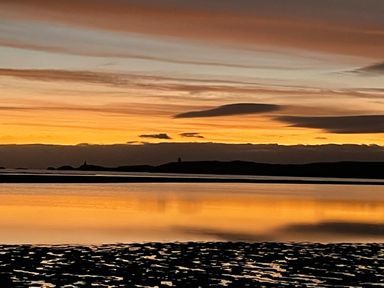 A sunset over a body of water with reflections and land in the distance at Barn End 9 Stad Clynnog Newborough