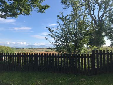 A garden with a wooden fence trees and a field in the background at Barn End 9 Stad Clynnog in Newborough