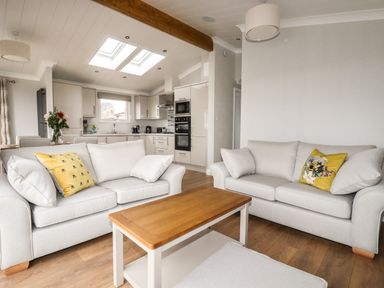 A living room with two sofas a wooden coffee table and a kitchen with skylights at Acorn Lodge in St Day