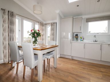 A kitchen and dining area with a wooden table set with flowers and chairs near windows at Acorn Lodge in St Day