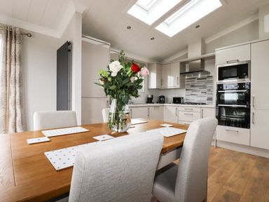 A kitchen and dining area with wooden table, chairs, flowers in a vase, and modern appliances at Acorn Lodge in St Day