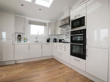 A kitchen with white cabinets wooden floor a window a microwave oven and a heater at Acorn Lodge in St Day