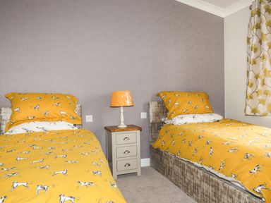 A bedroom with two single beds yellow dog patterned bedding a small nightstand with a lamp and floral curtains at Acorn Lodge in St Day