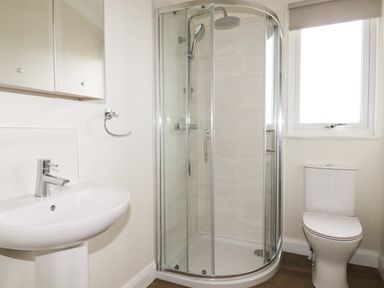 A bathroom with a sink and faucet a glass enclosed shower and a toilet near a window at Acorn Lodge in St Day