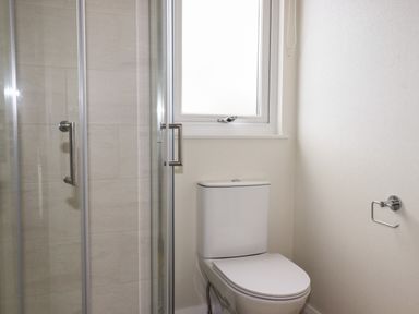 A bathroom with a toilet and a glass shower enclosure next to a window at Acorn Lodge in St Day