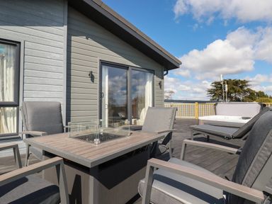 An outdoor patio with chairs around a fire pit table and a hot tub on a deck at Acorn Lodge in St Day