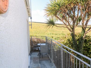 A small outdoor balcony with a round table and two chairs overlooking a grassy field and a tree at Perran Pearl A in Perranporth