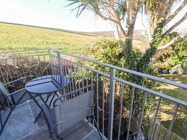 A balcony with two chairs and a round table overlooking a field and trees at Perran Pearl A in Perranporth