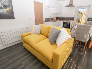 A yellow sofa with cushions in a living area adjacent to a kitchen and dining table with chairs at Perran Pearl A in Perranporth