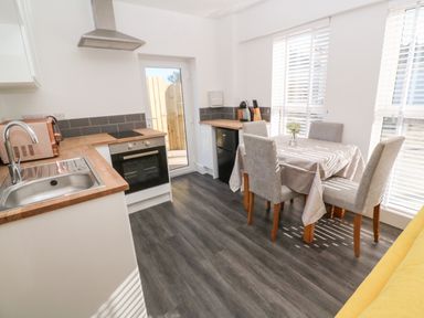 A kitchen with a dining table and four chairs next to windows with blinds at Perran Pearl A in Perranporth
