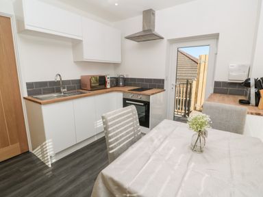 A kitchen with white cabinets a wooden countertop a dining table with a tablecloth and chairs and a glass door at Perran Pearl A in Perranporth