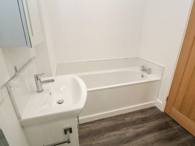 A bathroom with a white bathtub a white sink with a faucet and a wooden door at Perran Pearl A in Perranporth