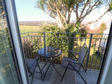 A small balcony with two chairs and a round table overlooking a garden with trees and fields at Perran Pearl A in Perranporth