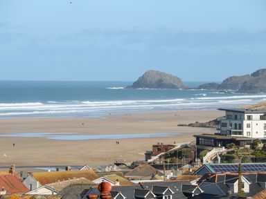 A beach with waves and rock formations in the sea and buildings in the foreground at Perran Pearl A in Perranporth
