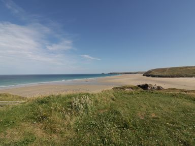 A beach with a grassy foreground and ocean under a blue sky at Perran Pearl B in Perranporth