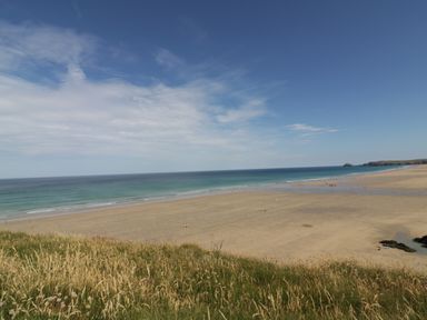 A sandy beach with grass in the foreground and the ocean in the background at Perran Pearl B in Perranporth