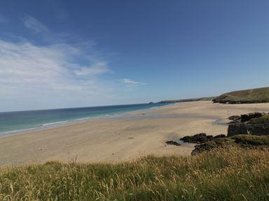 A sandy beach with people, grassy cliffs in the foreground, and a clear blue sky at Perran Pearl B in Perranporth