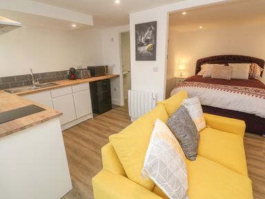 A studio apartment with yellow sofa and kitchen area next to a bed at Perran Pearl B in Perranporth