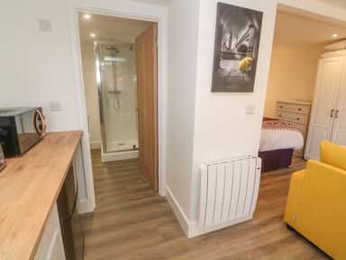 A small kitchen area with a microwave and wooden countertop next to a bathroom with a shower and a bedroom with a bed and wardrobe at Perran Pearl B in Perranporth
