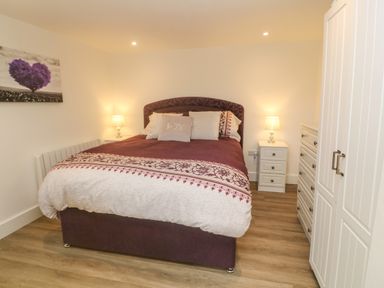 A bedroom with a double bed two bedside tables with lamps a chest of drawers a wardrobe and a wall painting at Perran Pearl B in Perranporth
