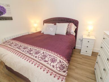 A bedroom with a bed covered in a patterned quilt bedside tables with lamps and a chest of drawers at Perran Pearl B in Perranporth