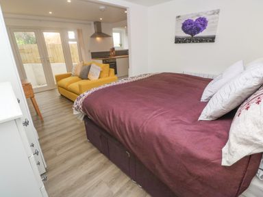 A bedroom with a purple bed cover and white pillows a yellow sofa and a kitchen area with glass doors at Perran Pearl B in Perranporth