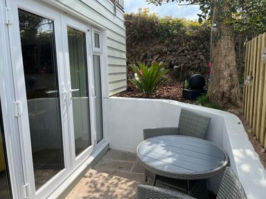 A small outdoor patio area with a round table and two chairs next to white double doors at Perran Pearl B in Perranporth