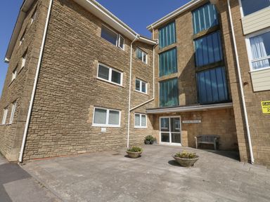 A brick apartment building entrance with potted plants and a bench at Chesil House in West Bay