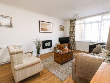 A living room with armchairs a sofa a wooden coffee table a television and a wall-mounted electric fireplace at Beach Side in West Bay