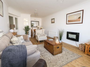 A living room with a sofa armchair wooden chest as coffee table wall-mounted fireplace and dining table at Beach Side in West Bay