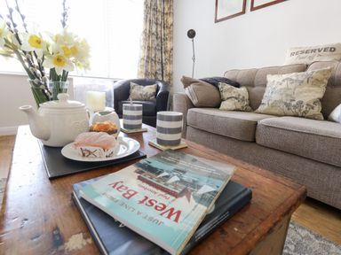 A living room with a wooden coffee table holding a teapot cups pastries books and a vase of flowers at Beach Side in West Bay